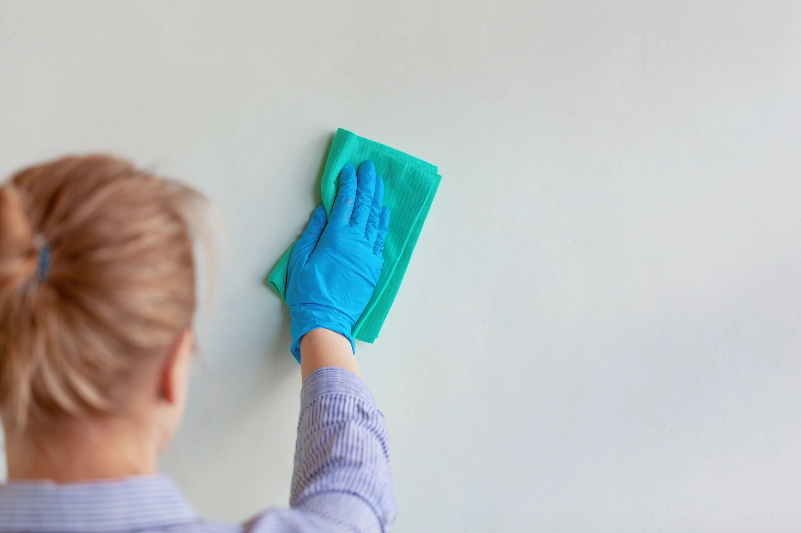 Employee hand blue rubber protective glove wiping wall from dust with rag